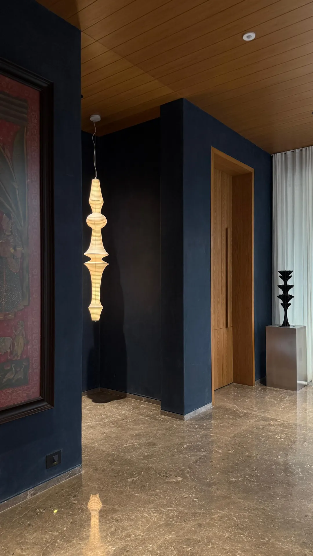 The same kind of hall handed over: a deep blue wall, a lit sculpture, the door.