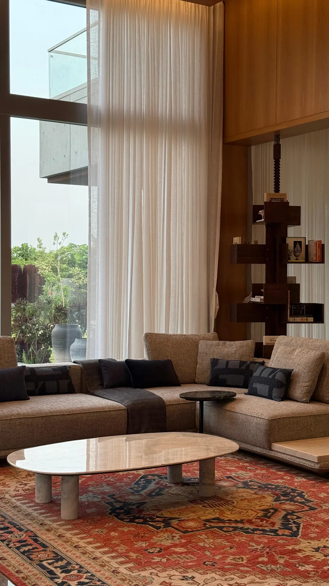 A living room handed over: glass to the garden, sofas on a rug.