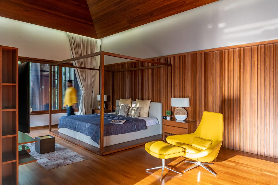 A bedroom in timber, a yellow chair by the glass.